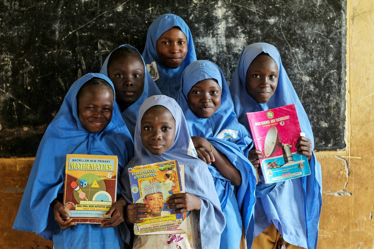 Schoolgirls in blue hijabs smiling and holding their books